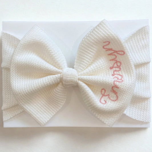 White bow headband with embroidered name on a white background